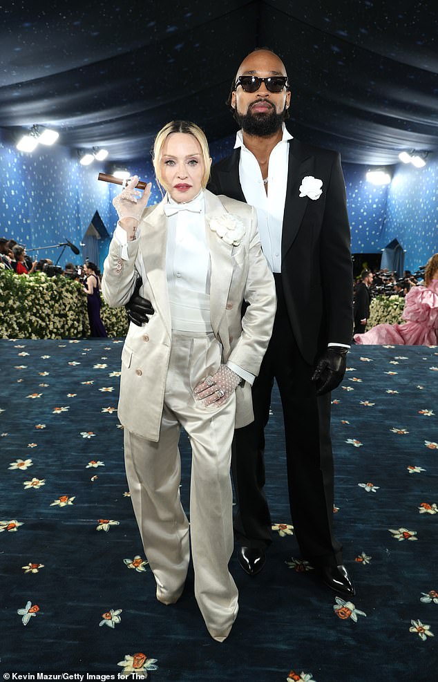 Madonna kept it simple in a silky pearl hued suit with a skintight white blouse and bow tie; she arrived with her toy boy lover Akeem Morris، who is 37 years younger than her