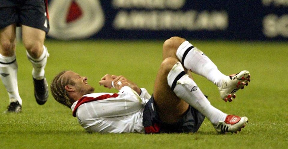 David Beckham on the ground holding his injured arm during a soccer game.