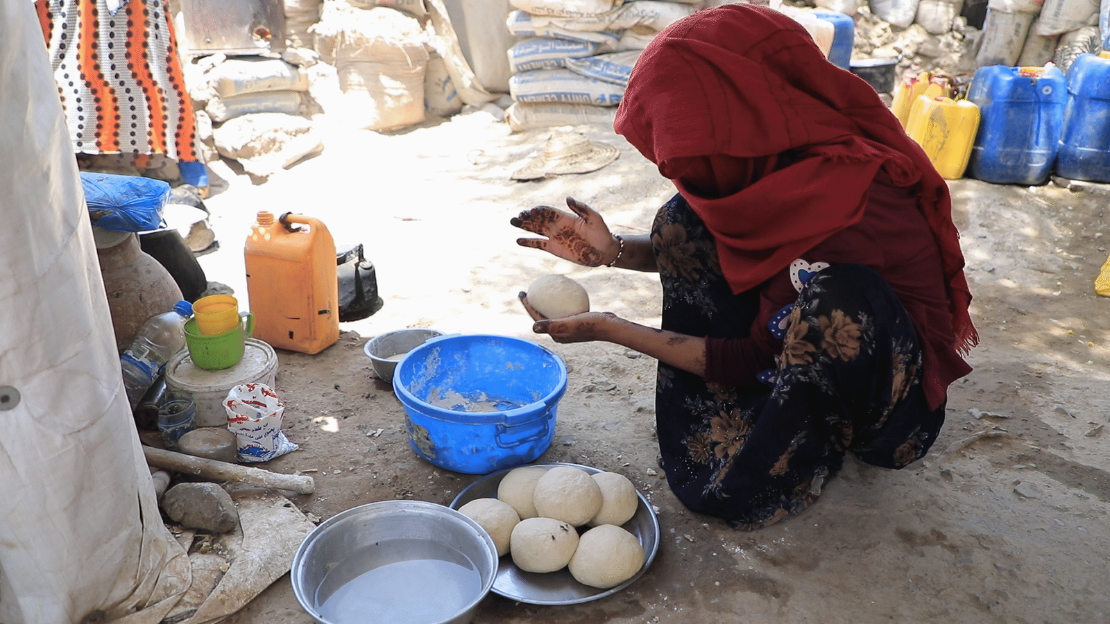 امرأة في مخيم لللاجئين في تعز جاثية على الأرض تعد خبزا