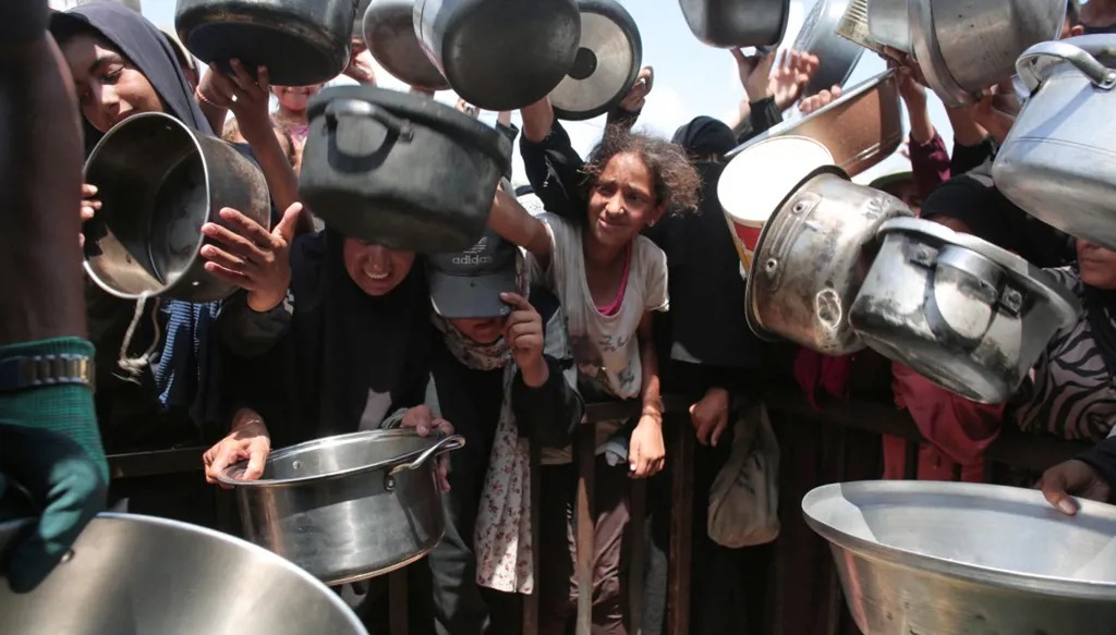 نساء وأطفال فلسطينيون يحملون أوانيهم الفارغة أمام مطبخ خيري في خان يونس (أ ف ب).
