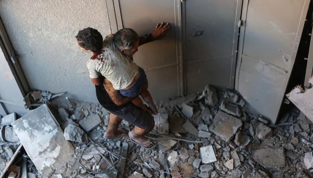 رجل فلسطيني يحمل طفلاً مصاباً من داخل مبنى استُهدف بغارة إسرائيلية في حي الرمال بمدينة غزة، في 30 آب 2025. (أ ف ب)